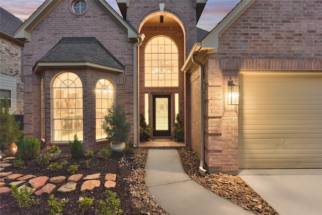doorway to property featuring a garage, concrete driveway, and brick siding