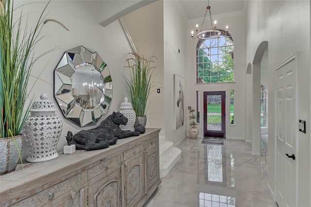 foyer with a towering ceiling, crown molding, arched walkways, marble finish floor, and an inviting chandelier