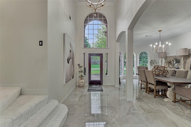 foyer with a towering ceiling, arched walkways, baseboards, marble finish floor, and a notable chandelier