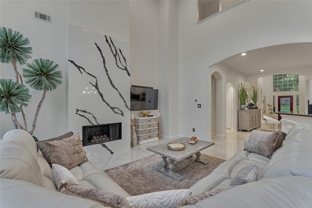 living room featuring arched walkways, marble finish floor, baseboards, a towering ceiling, and visible vents