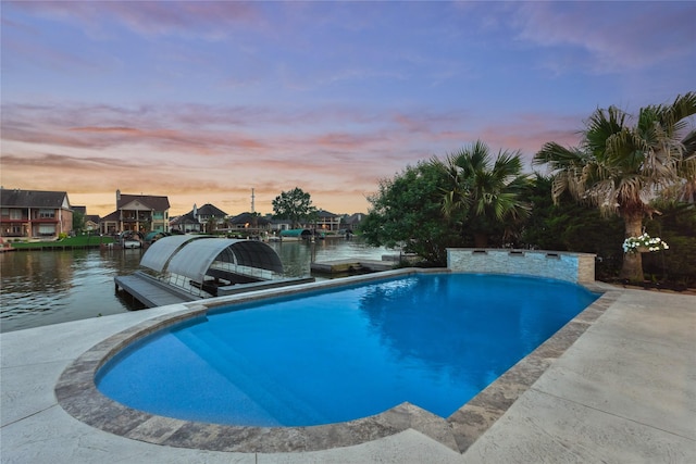 pool at dusk with a water view, an outdoor pool, and a dock