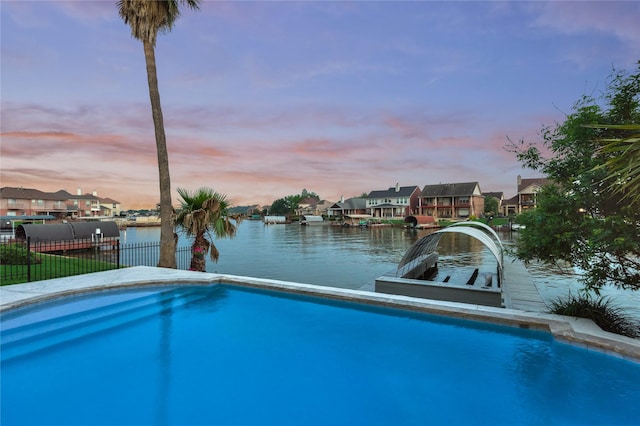 pool at dusk with fence, a water view, and a residential view