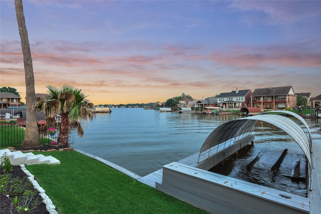 view of dock featuring fence, a water view, a yard, and a residential view