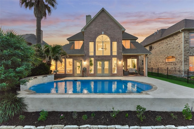 back of house featuring french doors, a chimney, brick siding, fence, and a fenced in pool