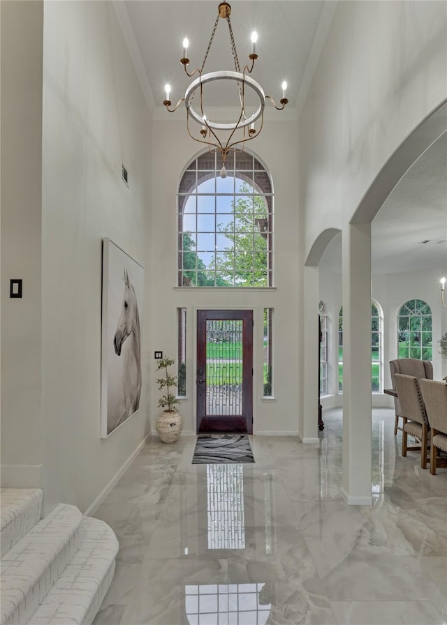 foyer featuring ornamental molding, a towering ceiling, arched walkways, and a notable chandelier