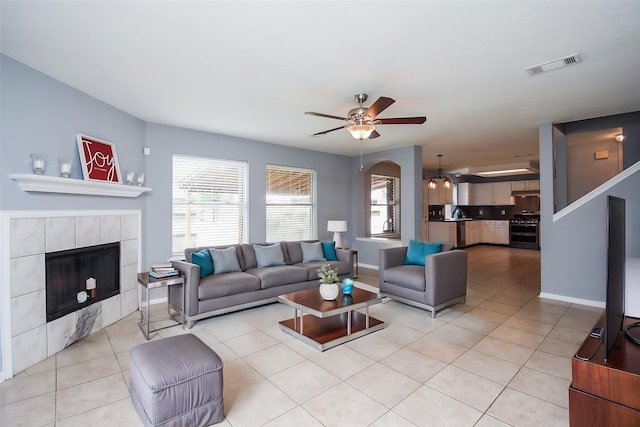 living room featuring ceiling fan, baseboards, light tile patterned floors, a tile fireplace, and visible vents