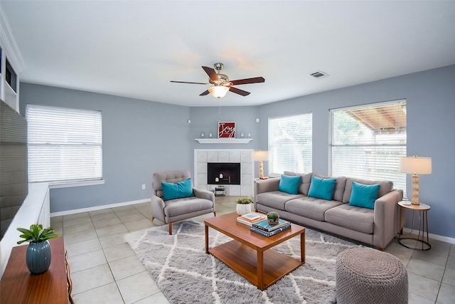 living area featuring visible vents, a fireplace, baseboards, a ceiling fan, and light tile patterned floors
