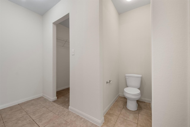 bathroom with tile patterned flooring, baseboards, a spacious closet, and toilet