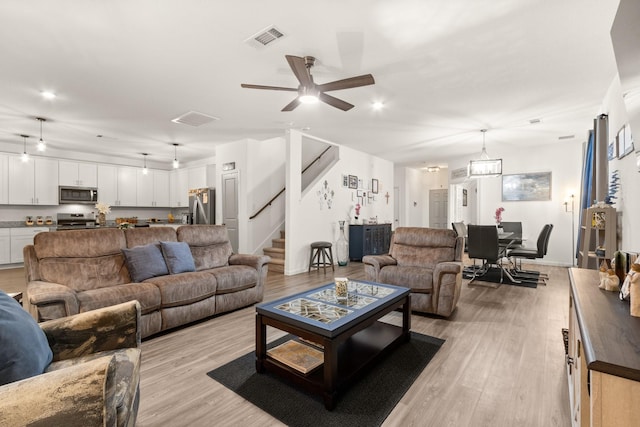 living room featuring stairway, ceiling fan, light wood-type flooring, and visible vents