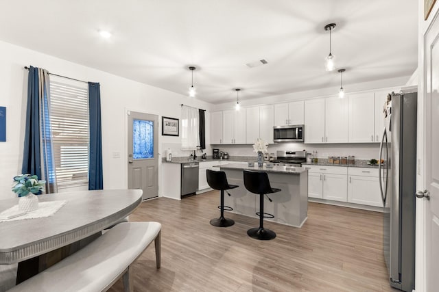 kitchen with visible vents, a kitchen island, a kitchen breakfast bar, white cabinetry, and stainless steel appliances
