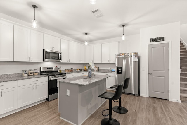 kitchen with appliances with stainless steel finishes, white cabinets, a kitchen bar, and light wood-type flooring