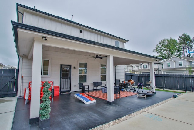 rear view of property featuring a patio, ceiling fan, board and batten siding, and fence