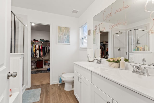 bathroom with a sink, toilet, a shower stall, wood finished floors, and visible vents