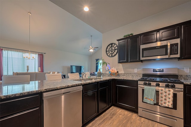 kitchen featuring light stone countertops, vaulted ceiling, a sink, stainless steel appliances, and light wood-style flooring