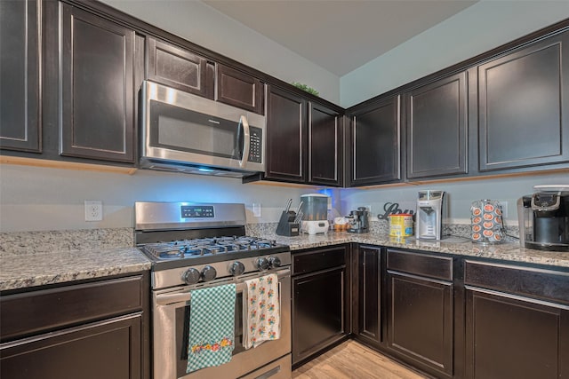 kitchen with light wood-style flooring, dark brown cabinetry, light stone countertops, and stainless steel appliances