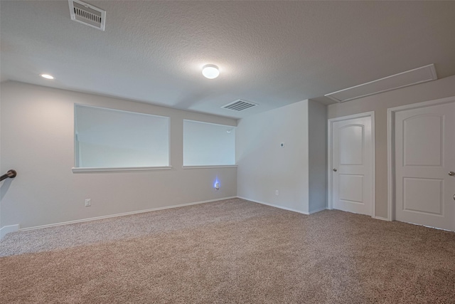 spare room with attic access, a textured ceiling, visible vents, baseboards, and carpet flooring