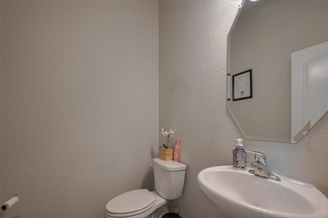 bathroom with toilet, a textured wall, and a sink