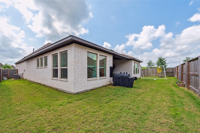 back of property with brick siding, a fenced backyard, a yard, and cooling unit