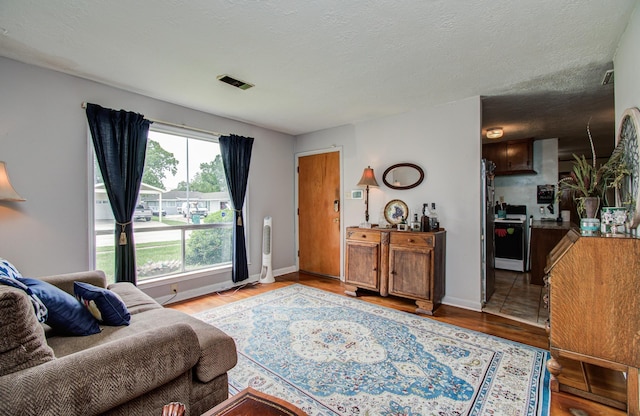 living area with a textured ceiling, baseboards, visible vents, and wood finished floors