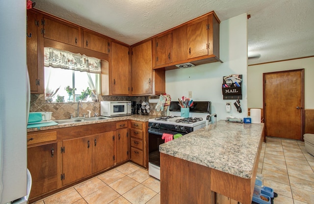 kitchen featuring a sink, white appliances, a textured ceiling, brown cabinetry, and a peninsula