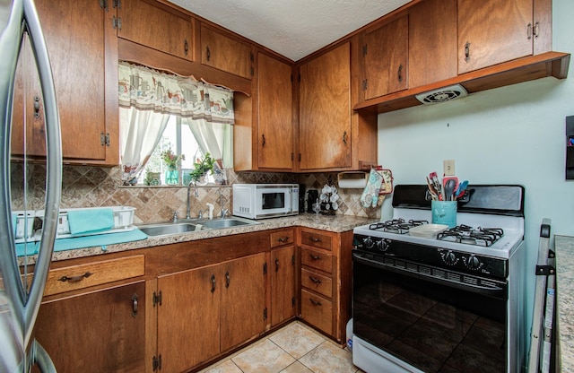 kitchen with white microwave, stainless steel refrigerator, a sink, gas stove, and tasteful backsplash