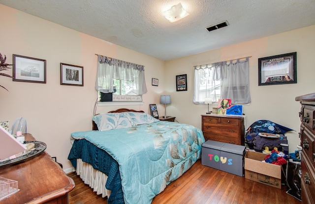 bedroom with a textured ceiling, visible vents, and hardwood / wood-style floors