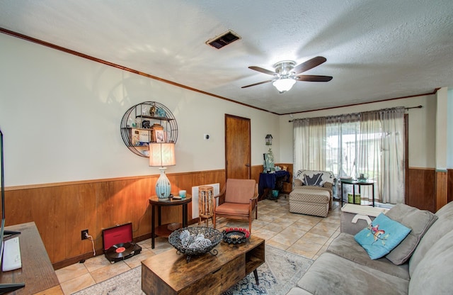 living room with wood walls, a wainscoted wall, a ceiling fan, light tile patterned floors, and visible vents