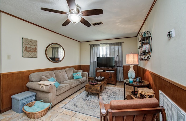 living area with ceiling fan, wood walls, a wainscoted wall, visible vents, and ornamental molding