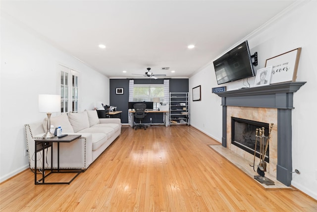 living area with a tiled fireplace, ornamental molding, ceiling fan, and wood finished floors