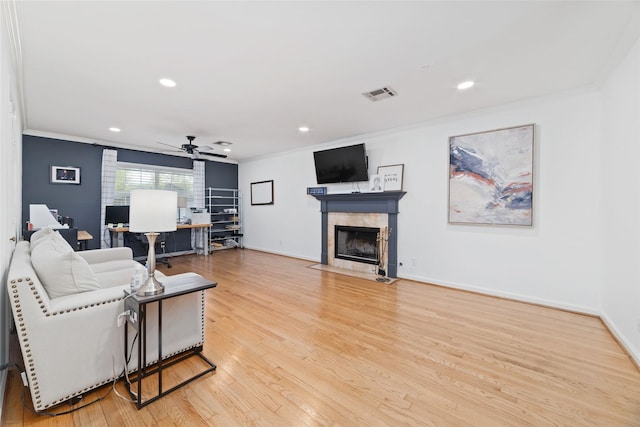 living area featuring crown molding, ceiling fan, light wood-style flooring, a tile fireplace, and visible vents