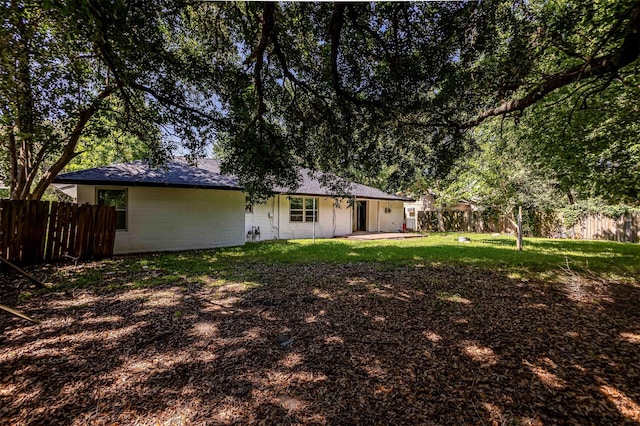 back of house with fence, a yard, a patio, a shingled roof, and concrete block siding