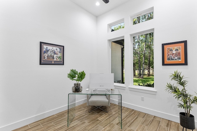 office area featuring baseboards, wood finished floors, and a towering ceiling
