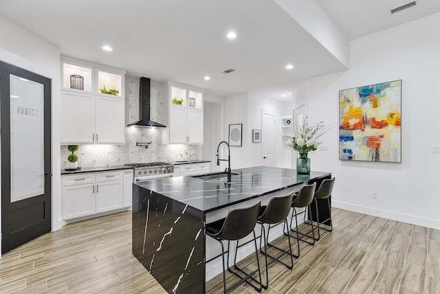kitchen featuring a sink, wall chimney range hood, light wood-style flooring, and visible vents