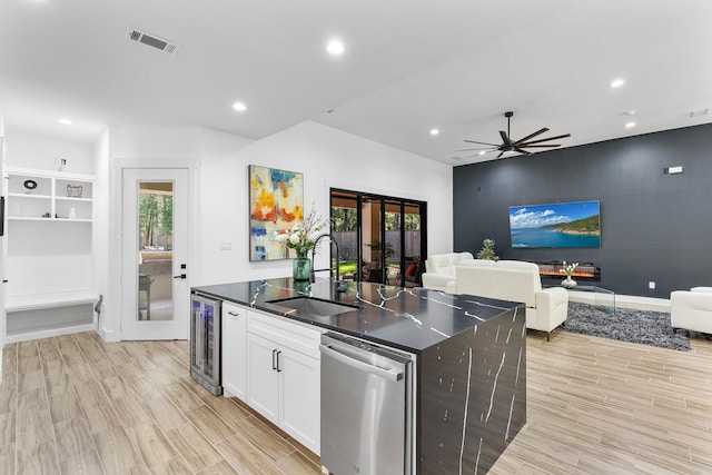 kitchen featuring visible vents, stainless steel dishwasher, a sink, beverage cooler, and an island with sink