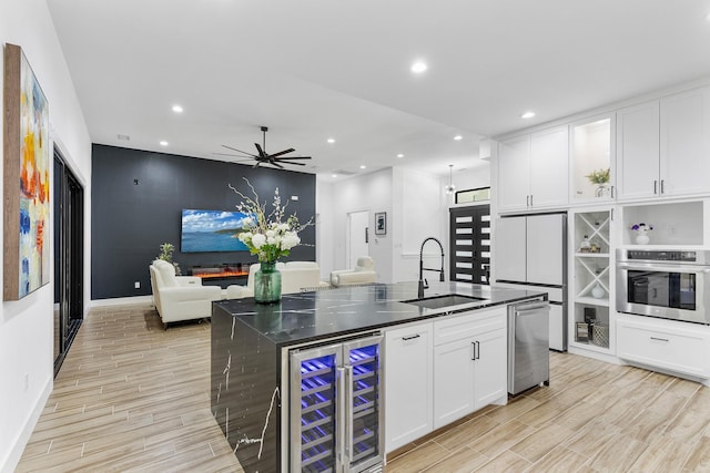 kitchen featuring white cabinets, appliances with stainless steel finishes, a sink, light wood-style flooring, and wine cooler