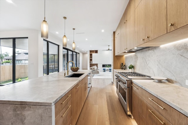 kitchen featuring a sink, light wood-style flooring, high end stove, a large island, and backsplash