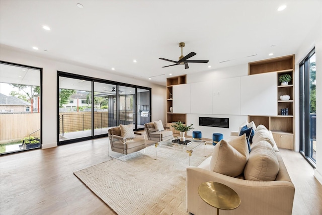 living room featuring recessed lighting, a ceiling fan, light wood finished floors, and plenty of natural light