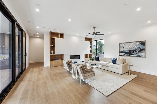 living room featuring a glass covered fireplace, baseboards, and light wood-type flooring