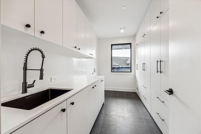 laundry area with cabinet space, a sink, baseboards, dark tile patterned flooring, and recessed lighting