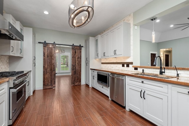 230009 Kama Dr, Porter, TX 77365 - kitchen with a barn door, wall chimney exhaust hood, tasteful backsplash, a sink, and appliances with stainless steel finishes