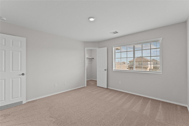 unfurnished bedroom featuring a walk in closet, visible vents, baseboards, a closet, and carpet