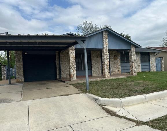 view of front of home featuring stone siding, a garage, a front yard, a carport, and driveway