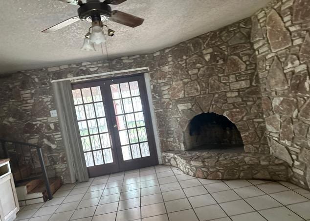 unfurnished living room with light tile patterned floors, plenty of natural light, french doors, and a textured ceiling