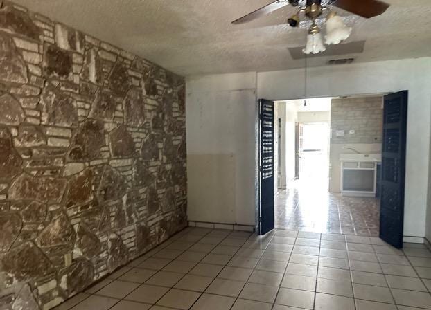 tiled spare room featuring a textured ceiling, ceiling fan, and visible vents