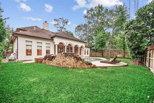 rear view of house with a lawn, a fenced backyard, roof with shingles, and stucco siding