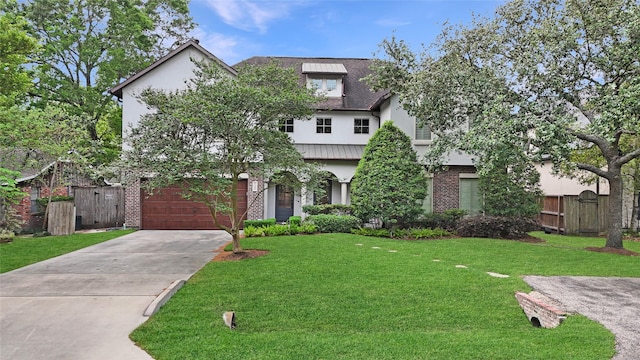 tudor house featuring fence, a front yard, stucco siding, an attached garage, and driveway