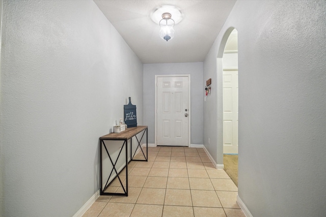 doorway with arched walkways, baseboards, and light tile patterned floors