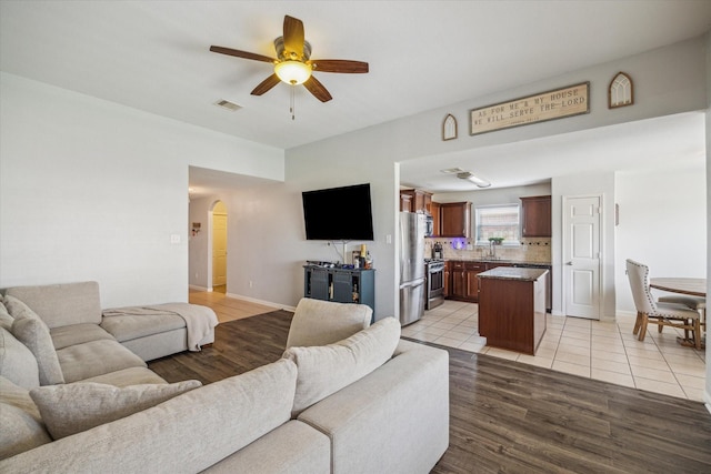 living area with arched walkways, a ceiling fan, baseboards, light tile patterned floors, and visible vents