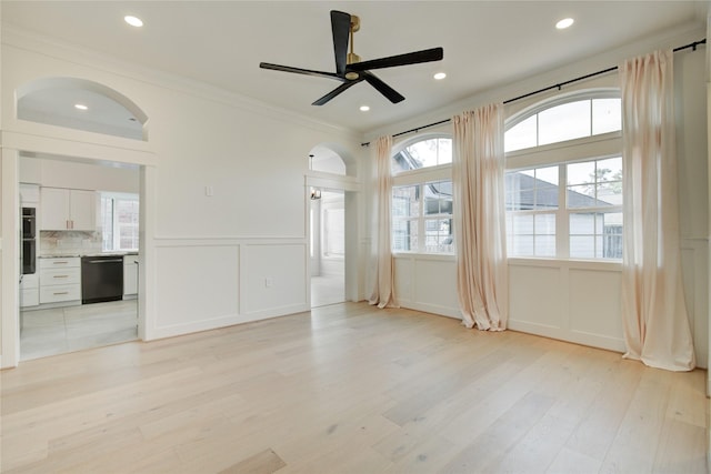 empty room with crown molding, a decorative wall, ceiling fan, a wainscoted wall, and light wood finished floors