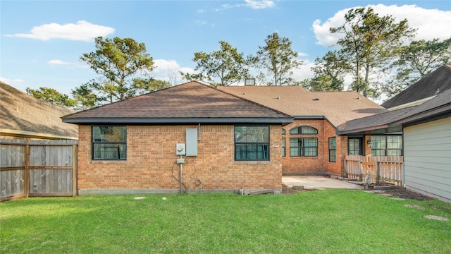 back of house featuring brick siding, a lawn, fence, and a patio